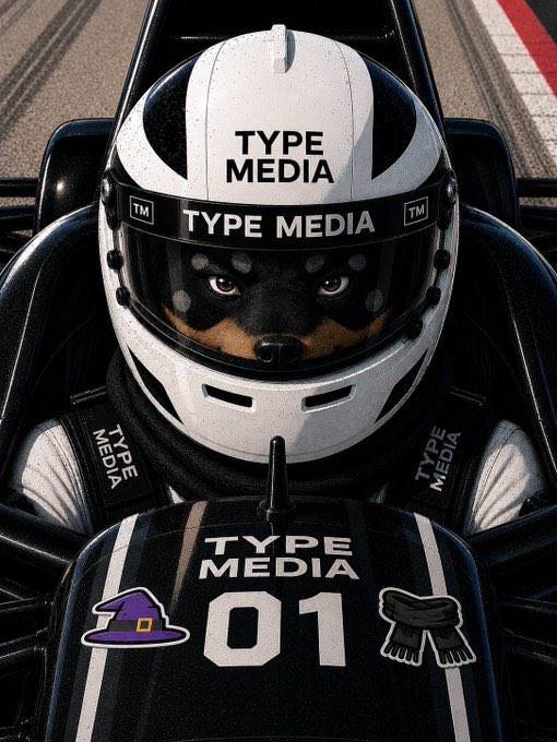 A close-up of a race car driver wearing a white "TYPE MEDIA" helmet with a dog's face visible through the visor, seated in a black race car with matching "TYPE MEDIA 01" branding and stickers.