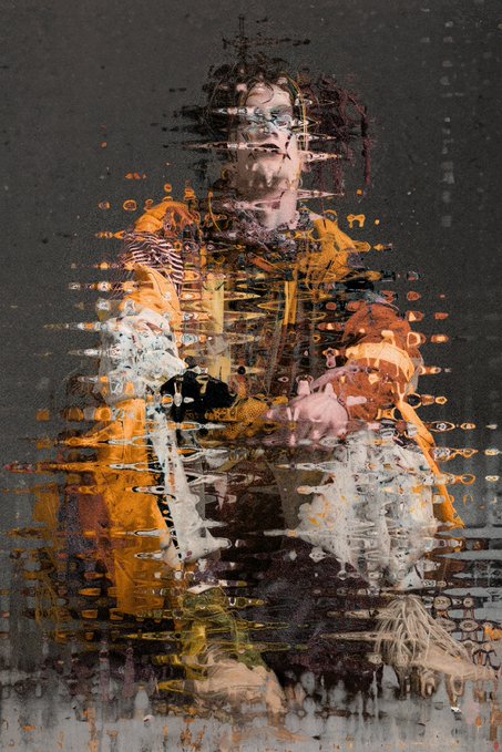 A glitch-effect portrait of a person wearing an orange jacket, with visual distortions and horizontal streaks of color across the image.