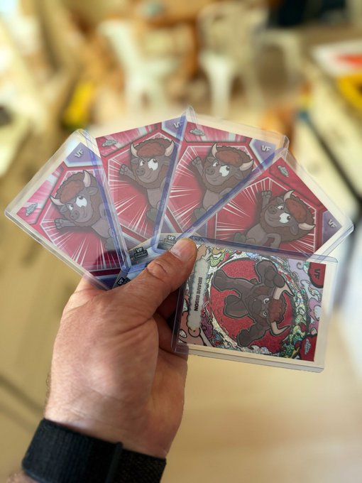 A hand fanning out multiple trading cards featuring a cartoon bull/bison character in pink sleeves, with one card showing a rabbit/hare character.