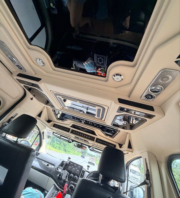 An interior view of a luxury vehicle looking up at a heavily customized, ornate ceiling with multiple panels, ambient lighting, and a panoramic sunroof.