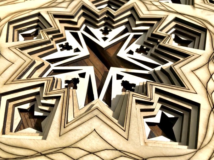 A close-up photograph of an intricately laser-cut wooden decorative object with star-shaped geometric patterns and layered designs.