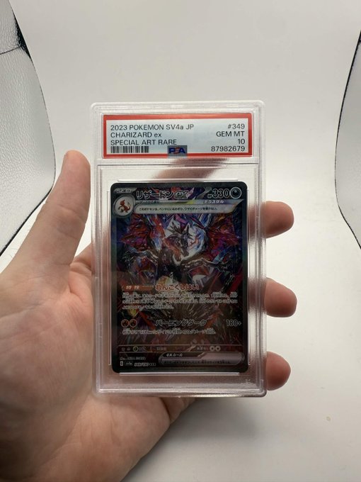 A hand holds a graded PSA GEM MT 10 trading card labeled '2023 POKEMON SV4a JP #349 CHARIZARD ex SPECIAL ART RARE', certified with barcode 87982679.