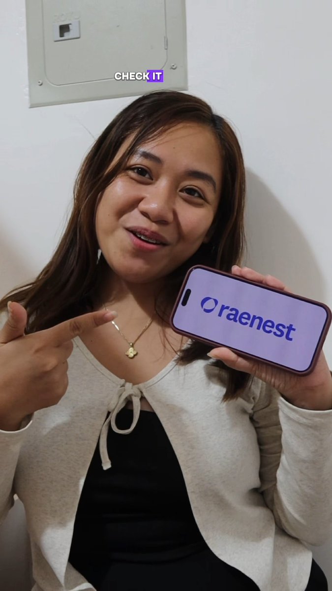 A selfie of a smiling woman with long brown hair pointing at her smartphone which displays the 'Oraenest' logo on a purple screen, with 'CHECK IT' text overlay.