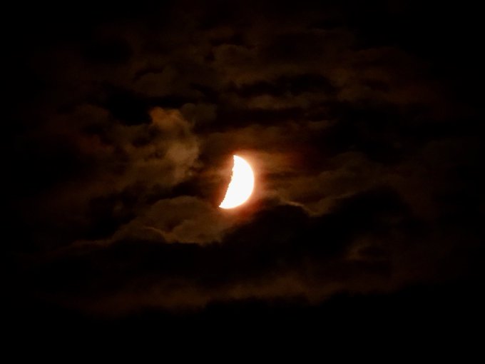 A glowing crescent moon shines through dark clouds in the night sky.