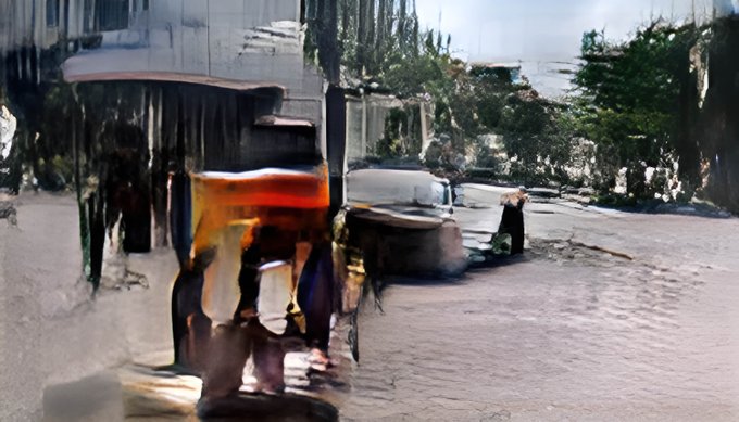 A blurry, distorted photograph showing what appears to be people near an orange/red vehicle or object on a street, with trees and a building in the background, though details are heavily obscured by visual artifacts.