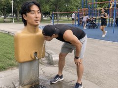 A humorous image showing a young man appearing to kiss the chest of a life-sized female mannequin torso in a park setting.