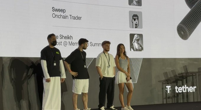 Four people stand on stage at what appears to be a Tether event, with a large screen behind them displaying profile cards labeled "Sweep, Onchain Trader" and "The Sheikh, Host @ Mem..." alongside the Tether logo, capturing a relaxed morning moment at the crypto gathering that fits the "Gm" greeting.