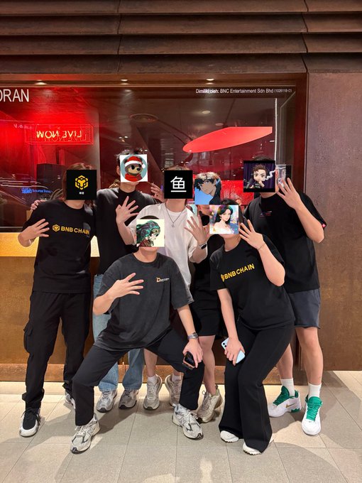A group of people wearing BNB Chain branded t-shirts pose together in front of a lit storefront, with their faces covered by various profile pictures including animal and human avatars.