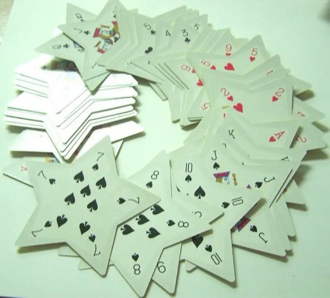 A scattered pile of playing cards fanned out on a white surface, showing various numbers and face cards from multiple suits including spades, hearts, and clubs.