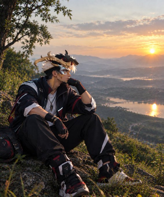 An anime-styled character cosplay photo of a white-haired figure with horn-like accessories, wearing a black and white jacket, sitting on a grassy hill overlooking a sunset landscape.