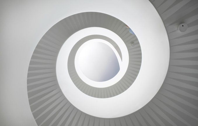 An artistic photograph taken looking straight up into a white spiral staircase, creating concentric circular patterns.