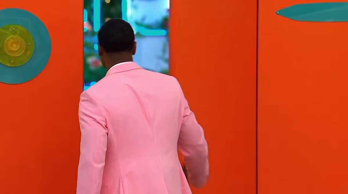 The image shows a man wearing a pink suit standing against an orange wall, with a green circle and a blue circle hanging above him. The man appears to be looking at something off-camera or towards the camera. The caption "sol tonight" suggests that this photo was taken during a recent event or gathering where people dressed up in formal attire were present.