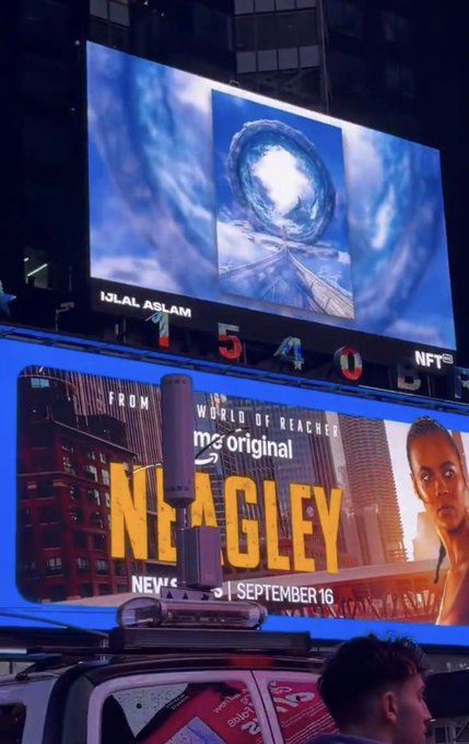 An outdoor digital billboard displays an artwork by 'IJLAL ASLAM' showing a portal over a pathway, positioned above an advertisement for the TV series 'REACHER' with 'NEAGLEY' premiering 'SEPTEMBER 16'.