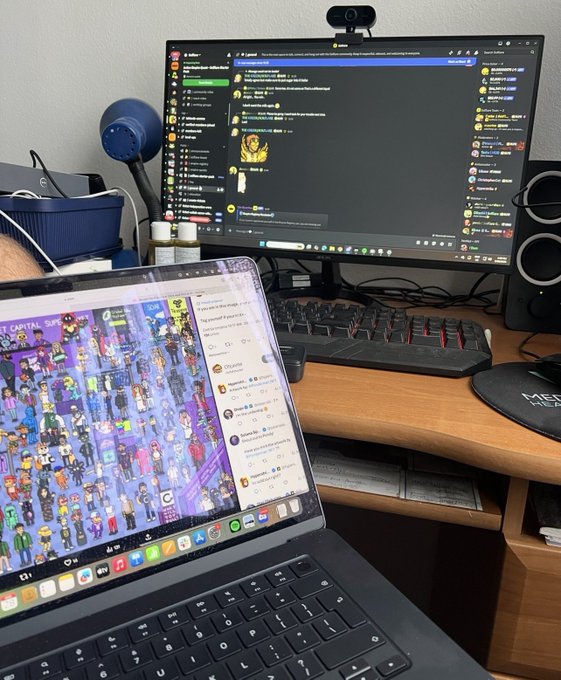 A dual-screen workspace displays a laptop showing an NFT collection called "Crystal Society" alongside a desktop monitor running Discord with the "Solflare Empire" server active, reflecting the user's active engagement in the Solana NFT community. The setup illustrates the digital hustle and multichannel involvement behind their commitment to "cooking hard" in the crypto space.