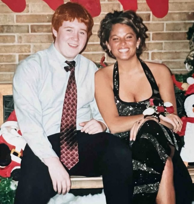 A red-haired young man in a white shirt and patterned tie sits beside a smiling woman in a black sequined halter dress, posed together at what appears to be a Christmas or winter formal event with festive decorations in the background. The caption reflects fans' excitement about the couple's relationship, speculating about how beautiful their future children would be.