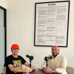 Two men sit at a table with microphones during a podcast recording at Bitcoin House MY, with one wearing an orange cap and "HODL" shirt, and a large framed Bitcoin reference poster displayed on the wall behind them.