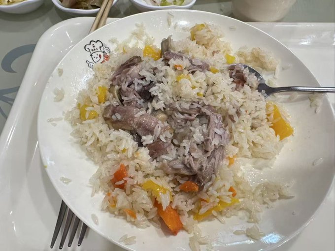 A plate of hand-pulled rice (手抓饭) topped with tender lamb pieces and colorful vegetables like carrots and yellow peppers, served with a fork on a white plate featuring a small chef logo. The dish reflects the Xinjiang cuisine the poster mentioned craving after arriving in Hami, with the promotional text about Binance's USD1 giveaway and affordable Hami melons also referenced in the post.