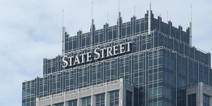 A tall glass skyscraper displaying the 'State Street' name and logo at the top of its facade against a partly cloudy sky.
