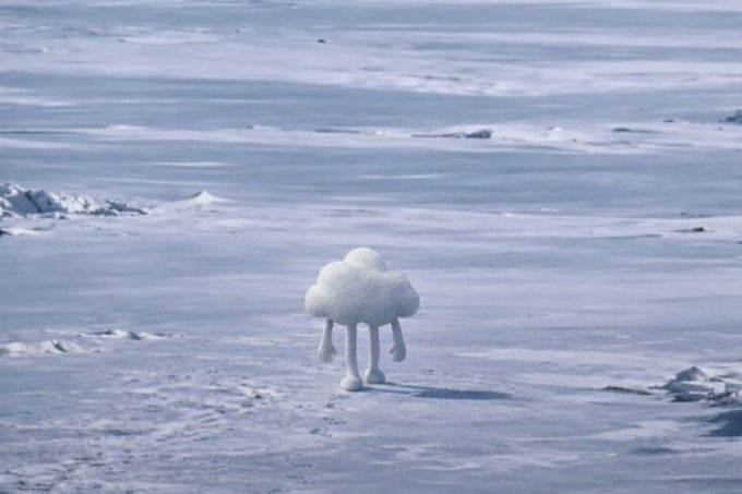 A whimsical white snow sculpture shaped like a cloud with stick legs standing in a vast, snowy landscape.