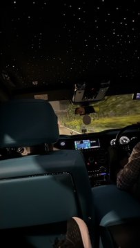 A view from the back seat of a luxury car at night, showing a starlight headliner roof and the dashboard display.