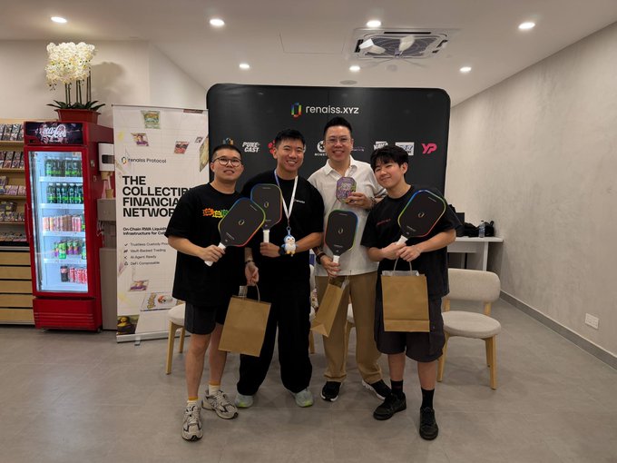 Four smiling young people pose indoors holding pickleball paddles and small shopping bags in front of a "renalss.xyz" banner and a "Financial Network" display stand.