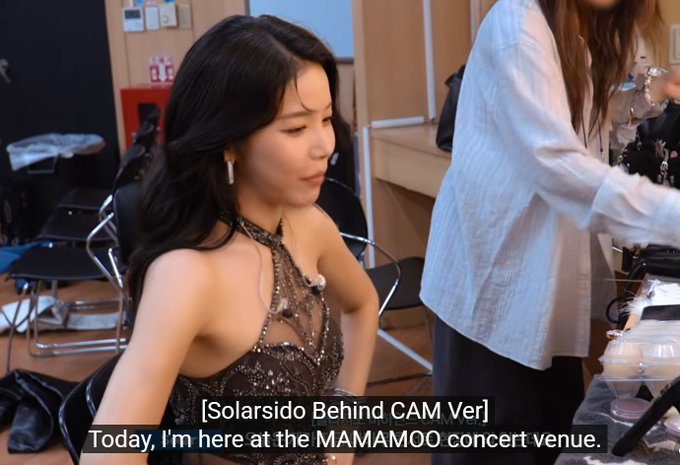 The image shows a young woman with long dark hair sitting in what appears to be a backstage area, wearing a sparkly black halter dress, with subtitles reading "[Solarsido Behind CAM Ver] Today, I'm here at the MAMAMOO concert venue."

The caption suggests a behind-the-scenes, "SOLARSIDO" (fan POV) perspective of a MAMAMOO concert, tying into the post's excitement about an immersive fan experience being made real.