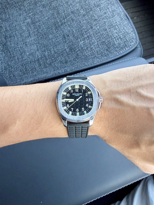 A person's wrist sports a silver-cased Navitimer wristwatch with a black dial and dark blue rubber strap.