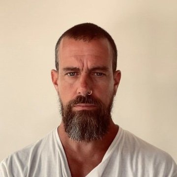 A serious-looking man with a short buzz cut, full beard, and septum piercing stares directly at the camera while wearing a white V-neck T-shirt against a plain beige background. The image likely represents Jack Dorsey, the Block CEO mentioned in the post about his company joining the x402 Foundation to contribute Bitcoin Lightning payments for an AI agent payment standard.