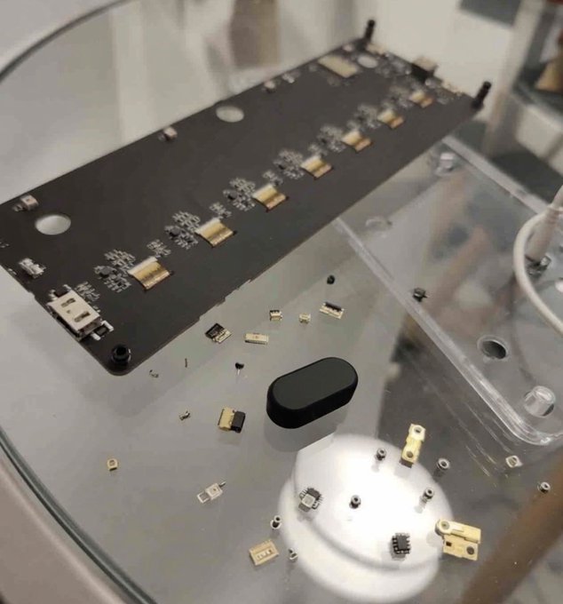 A disassembled "Block Clock" reveals its internal circuit board alongside scattered SMD components and a black oval-shaped speaker, claimed by the poster to be a secretive Russian GRU "Ухо-9" nano-acoustic listening device. The image shows no visible Russian markings or text to substantiate the claim, appearing instead as ordinary clock electronics.