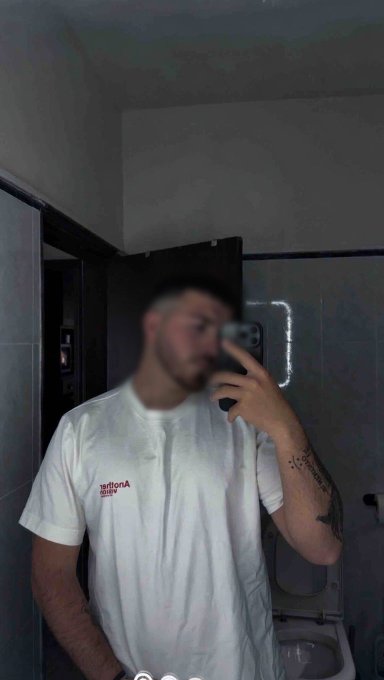 A man takes a mirror selfie in a bathroom while wearing a white t-shirt that reads "Arizona" (appearing mirrored); the casual morning photo complements his "Good Morning" post asking followers to drop their $SOL addresses.