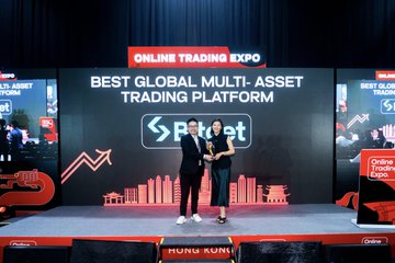 The image features two people standing next to each other with a podium between them, both holding a trophy. They are at an event called Online Trading Expo, where they have won an award for their achievement. The event takes place in Hong Kong, as indicated by the text on the image. The main focus of the image is the two individuals and their trophy, celebrating their success at the expo.