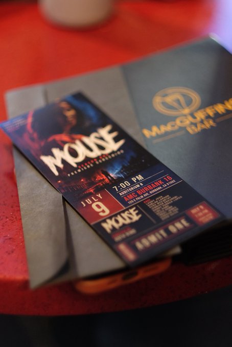 A promotional ticket for a concert by the band 'MOUSE' rests on a McGuffin's Bar coaster on a red table, advertising a July 9, 7:00 PM show in Southington, CT.