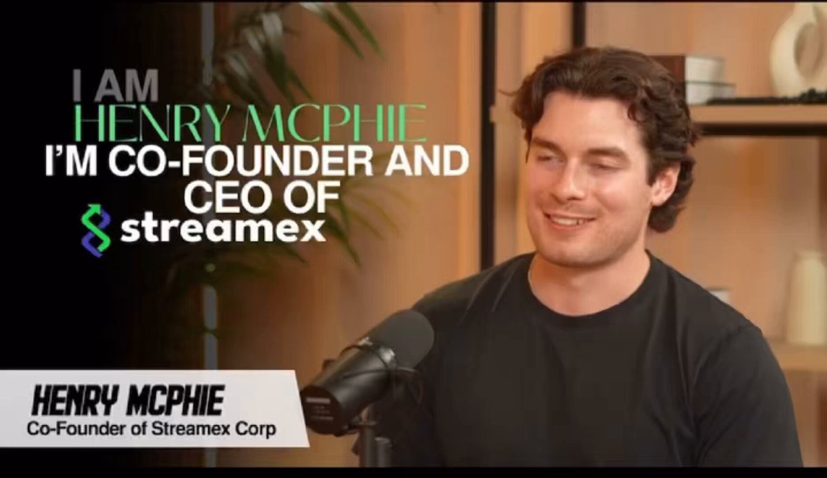 The image features a man wearing a black shirt, standing next to a microphone and speaking into it. The background of the image shows a wooden wall with a plant behind him. There are also some text elements present in the image that read "I AM Henry McPhie Co-Founder & CEO of Streamex".
