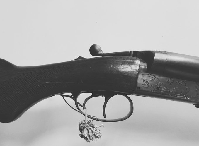 A close-up, black and white photograph of a shotgun's receiver, trigger guard, and part of the stock, featuring engraved floral designs on the metal.