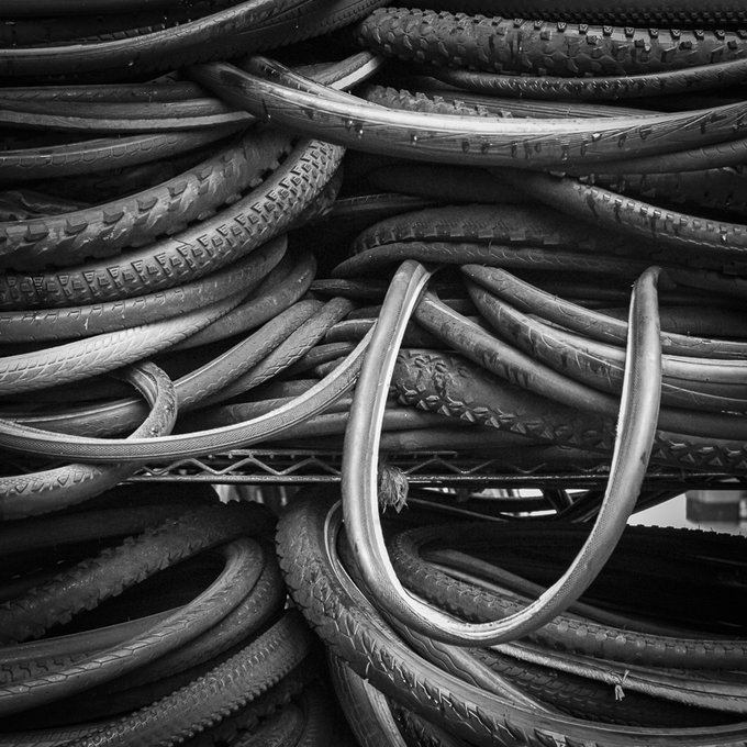A black and white close-up photograph of numerous bicycle tires stacked on a wire shelf.