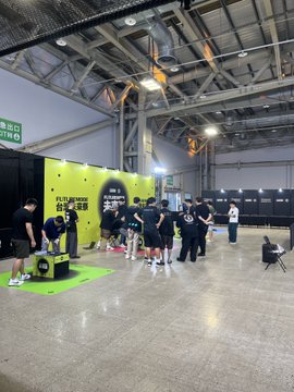 A group of people gathered in an indoor exhibition hall, standing near a booth with a bright green wall that reads "FUTURE NOW."
