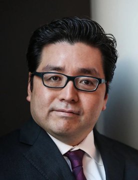 The image features an Asian man with glasses dressed in a suit and tie, standing against a dark background of textured wall or fabric. The caption reads "JUST IN: Tom Lee'S 'Bitmine' $ETH investment is currently at a $10,000,000,000 unrealized loss". This information seems unrelated to the main subject of the image. It appears that more context is needed before understanding the connection between the man in the suit and the post about Tom Lee's investment.