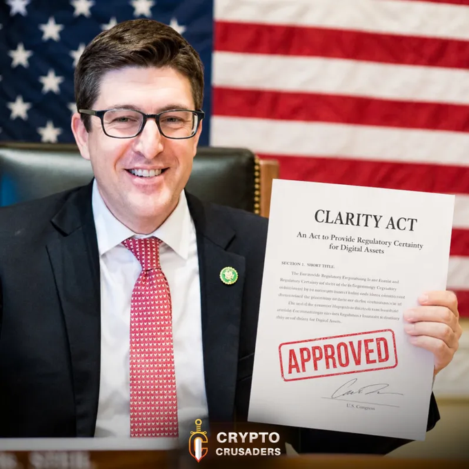 The image shows a smiling man in a dark suit, red patterned tie, and glasses holding up a document titled "CLARITY ACT: An Act to Provide Regulatory Certainty for Digital Assets" stamped with a red "APPROVED" seal, standing before an American flag. A "CRYPTO CRUSADERS" logo appears at the bottom right of the image. The image visually reinforces the post's message about Republican Bryan Steil's optimism that the Clarity Act will pass, framing it as an approved milestone for crypto and XRP.
