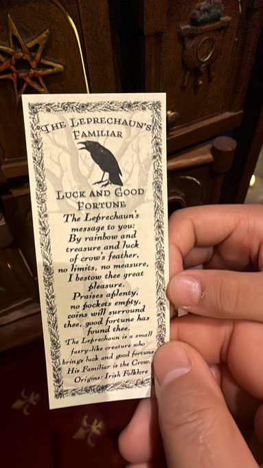 A hand holds a small card titled "The Leprechaun's Familiar" describing it as a "Luck and Good Fortune" charm with a poem about a fairy-like creature, set against a wooden background with decorative ornaments. The whimsical card appears unrelated to the post's content about setting up ether.fi and Plasma crypto wallet cards for visiting relatives in Australia.