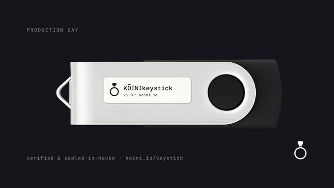 A silver USB hardware wallet labeled 'KÖINIkeystick v1.0 · koini.io' with text 'PRODUCTION DAY' and 'verified & sealed in-house · koini.io/keystick'.