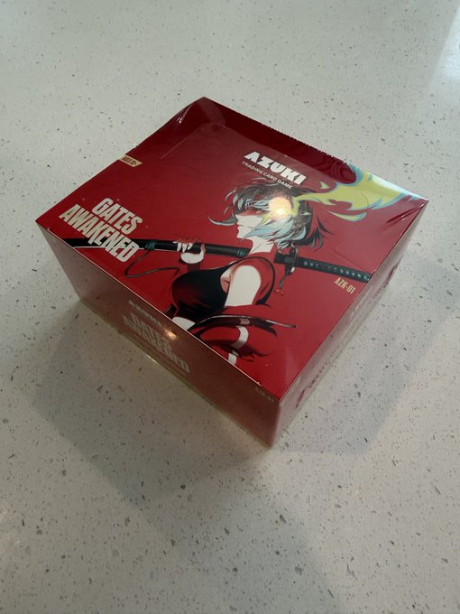 A red collector's edition box for the AZUKI trading card game 'FATE'S AWAKENED', featuring anime-style character artwork on a countertop.