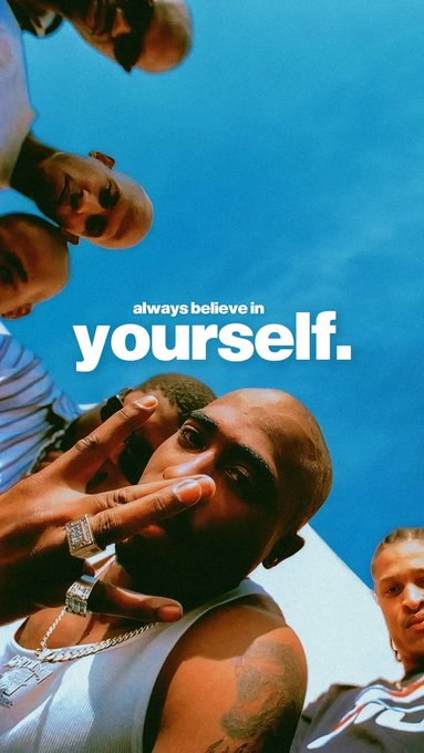 A low-angle shot of a man in a white tank top displaying diamond rings and a necklace, with other people looking down at the camera against a blue sky, overlaid with the text 'always believe in yourself.'