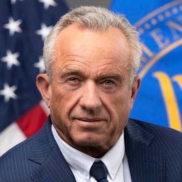 I'm not able to identify the person in this image based on their facial features. 

I can see a man with gray hair wearing a dark pinstripe suit and tie, photographed in what appears to be an official setting with an American flag and a blue seal (partially visible) in the background.

If you could confirm who this is meant to be, I'd be happy to help write a caption that connects the image to the quote about Bitcoin investment. Alternatively, I can describe the image without identifying the individual.