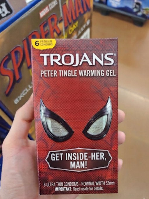 A hand holds up a red box of 'TROJANS' condoms labeled 'PETER TINGLE WARMING GEL', with a Spider-Man display visible in the background.