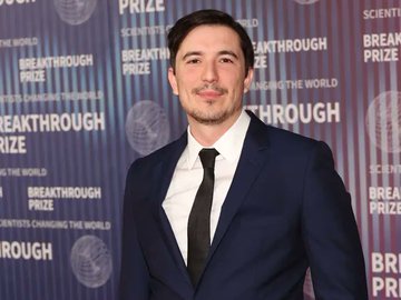 A man in a dark suit and tie stands in front of a backdrop reading 'BREAKTHROUGH PRIZE' and 'SCIENTISTS CHANGING THE WORLD.'
