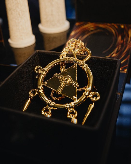 A detailed gold pendant featuring the Eye of Truth from Fullmetal Alchemist rests in a black display box.