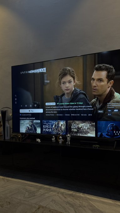 A large flat-screen TV displays an HBO Max interface featuring the movie 'Interstellar' with characters in space suits visible on screen, mounted above a dark console.