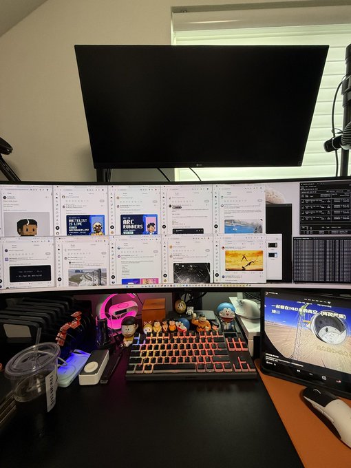 A complex multi-monitor computer setup displaying Twitter feeds, with figurines, a mechanical keyboard, and a smaller screen showing a video.