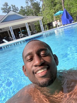 Kobe Bryant smiles while swimming in a bright blue pool, with a house and a blue umbrella visible in the background.