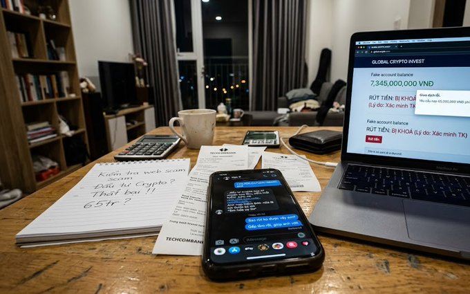 A desk scene showing a smartphone with a chat, a laptop displaying 'GLOBAL CRYPTO INVEST' and a '7,345,000,000 VNĐ' balance, a calculator, a coffee mug, and handwritten notes.